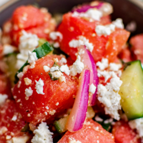 Watermelon salad in a bowl with feta salad, cucumbers and red onion.