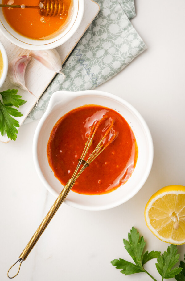 A bowl of red sauce with a whisk inside.
