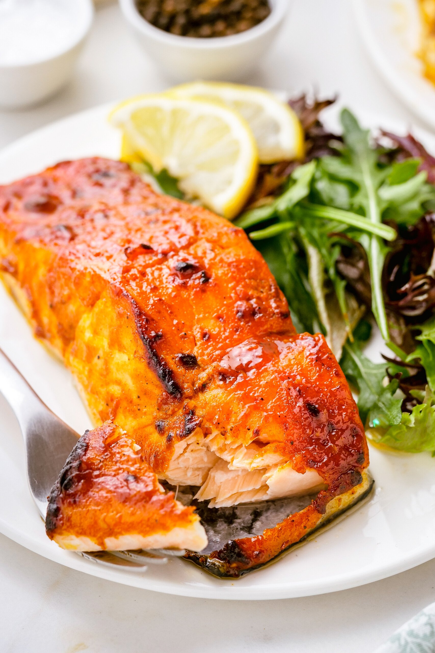 A fork breaking a bite of salmon away from a fillet.