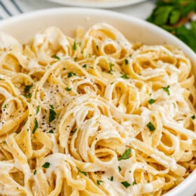 A white bowl of pasta in creamy sauce.