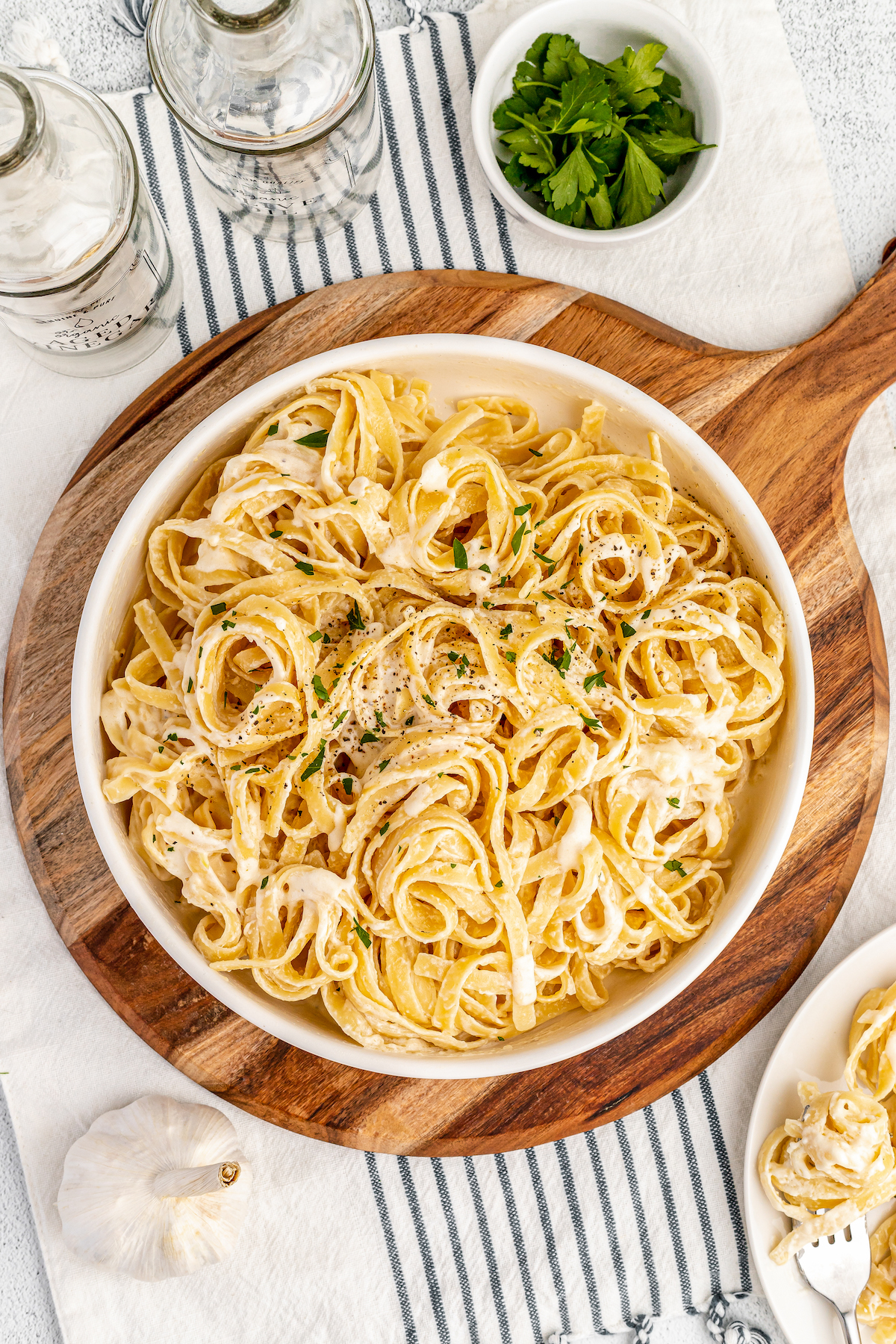 Creamy pasta garnished with parsley in a white dish, on a wooden cutting board.