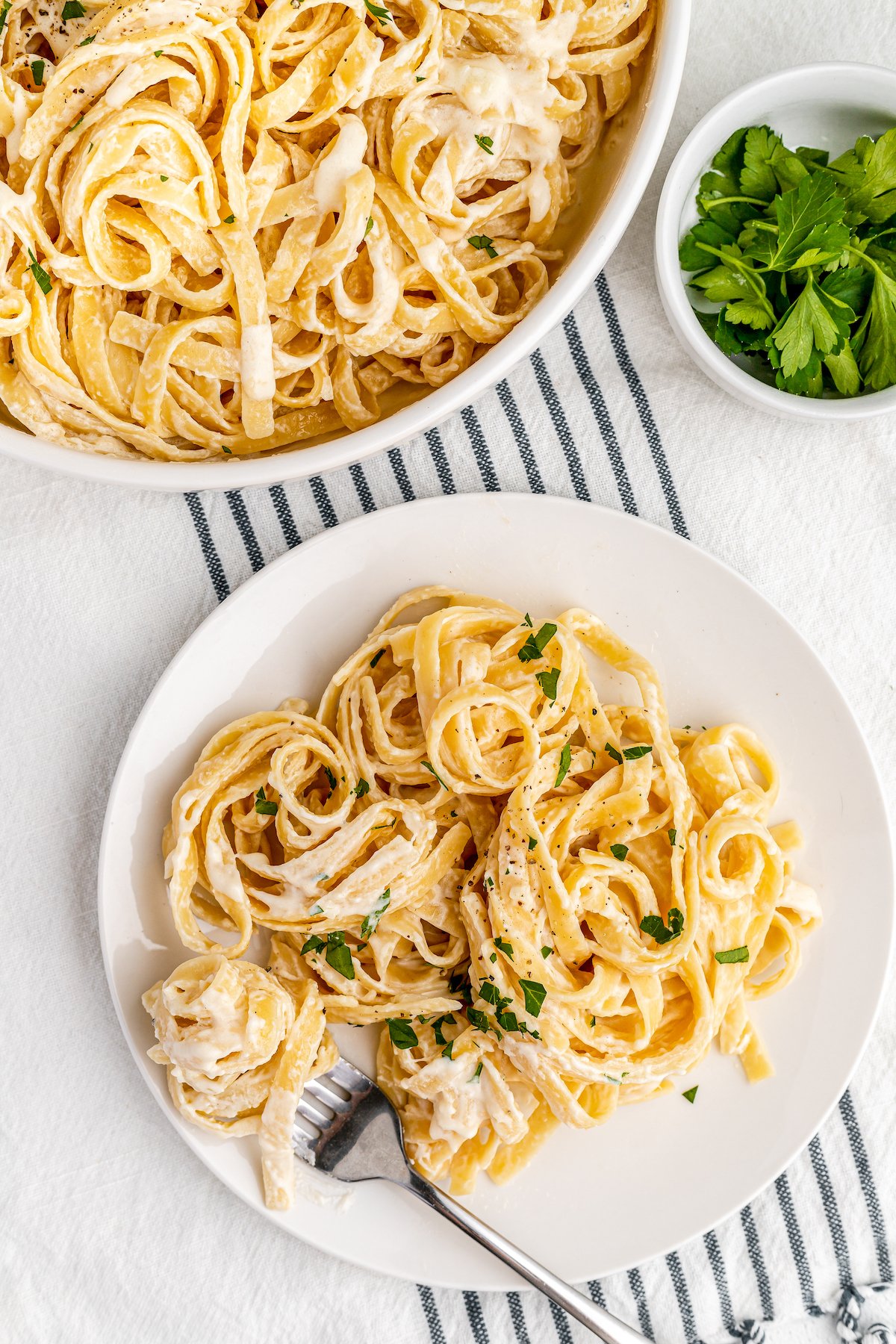 A table is set with a blue-ticking cloth, and a plate of pasta with a fork.