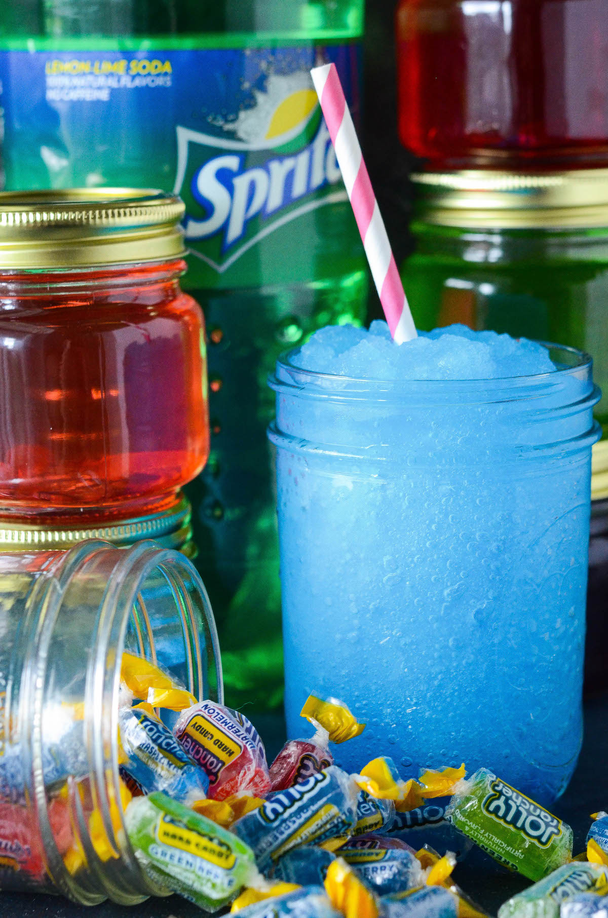 Jars of infused vodka with a blue vodka Slushies drink in a mason jar.