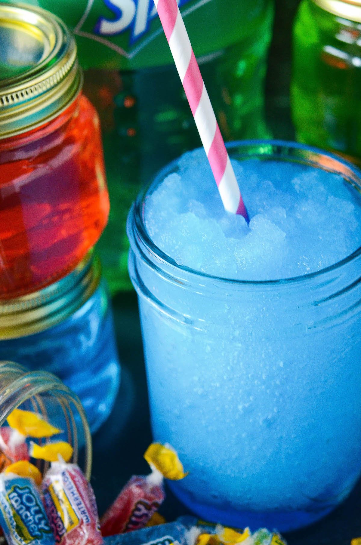 Blue vodka Slushies in a mason jar with a pink spoon and jolly rancher candies around the bottom of the glass.