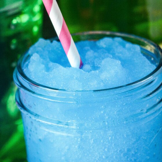 Up close image of a blue boozy slushie with a pink straw.
