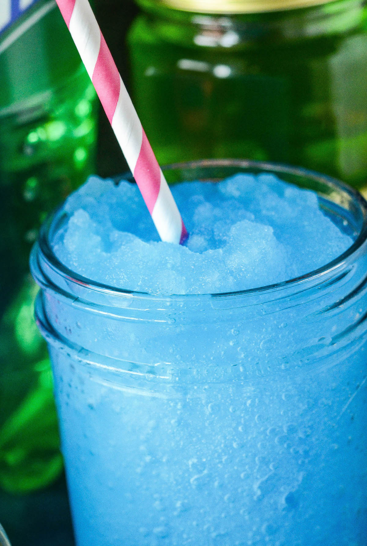 Up close image of a blue boozy slushie with a pink straw.