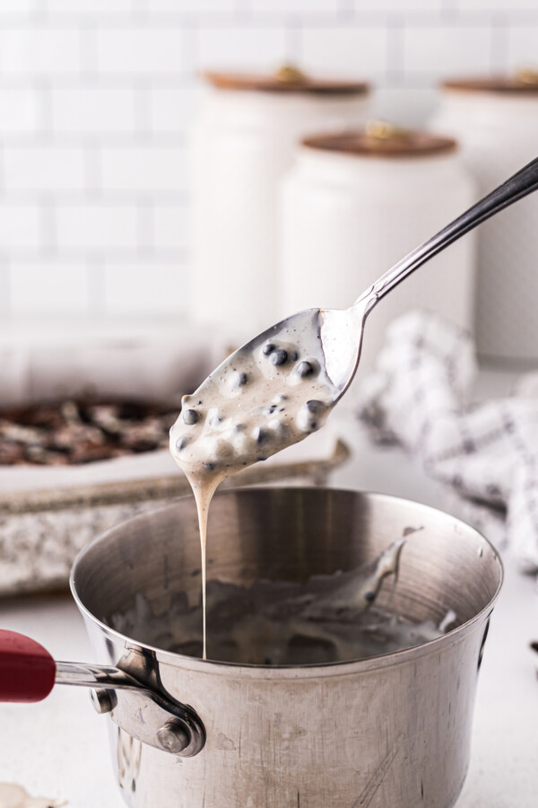 Melted cookies and cream candy bars in a small saucepan. Some of the melted candy is drizzling off of a spoon held above the saucepan.