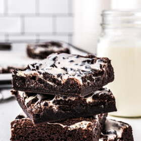 A stack of iced brownies on a countertop, with canisters of ingredients in the background.
