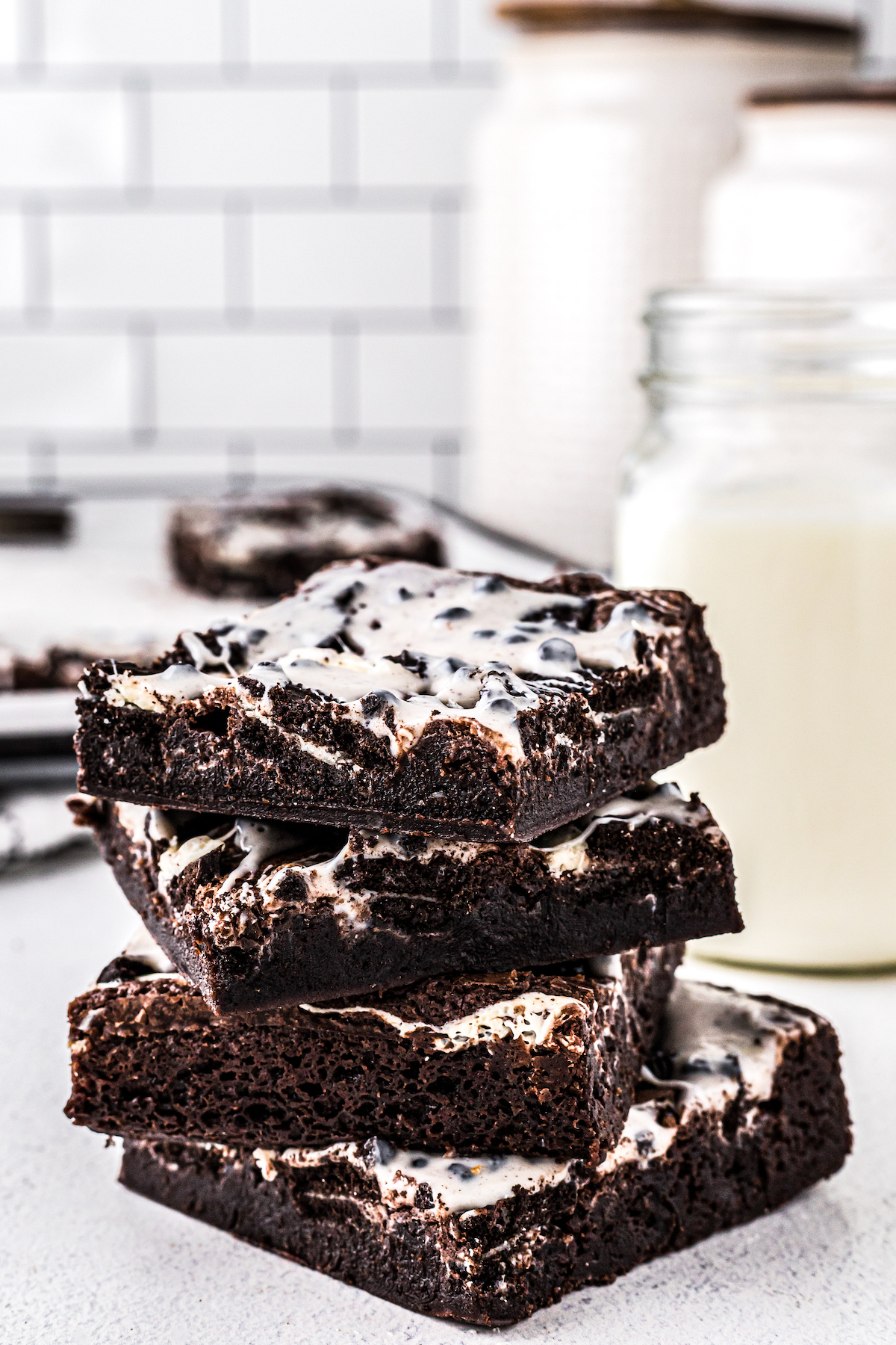 A stack of iced brownies on a countertop, with canisters of ingredients in the background.
