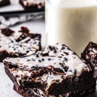 Brownies stacked around a tall mason jar of milk. One of the brownies has had a bite taken from it.