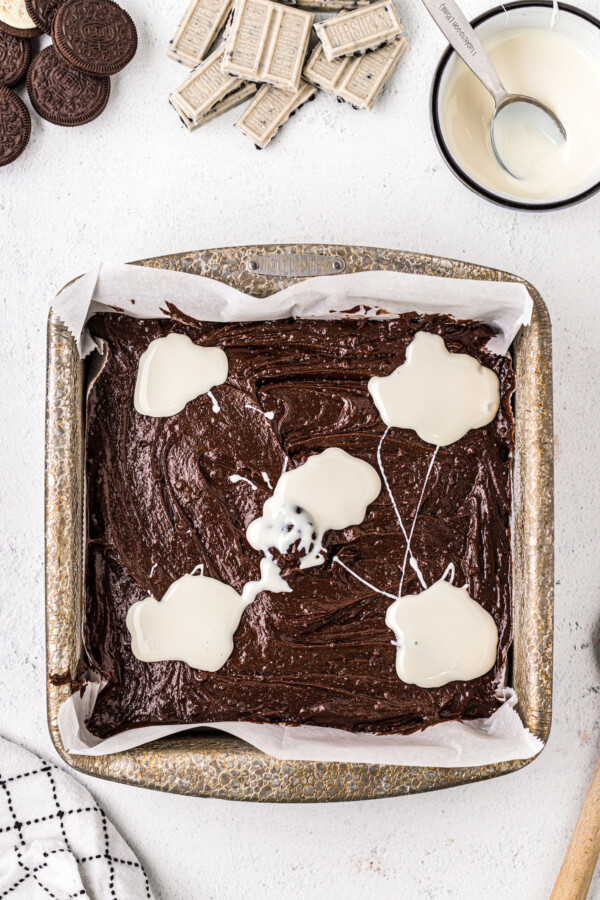 A metal baking pan filled with brownie batter, with dollops of marshmallow sauce on top.