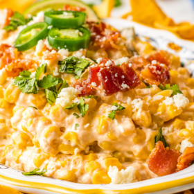 A bowl filled with corn dip with bacon on top and Frito chips.
