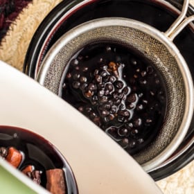 Elderberry syrup being drained with a sieve to remove the elderberries.