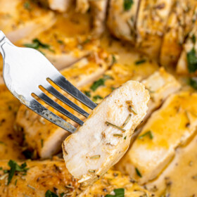 A fork lifting a piece of sliced chicken breast out of a baking dish of baked chicken.