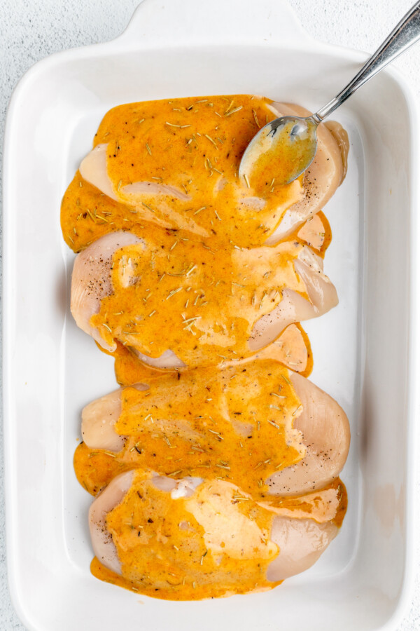 Raw chicken breasts in a dish, covered with sauce.