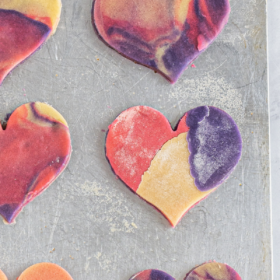 Sliced heart shaped marbled sugar cookie dough on a cookie sheet.