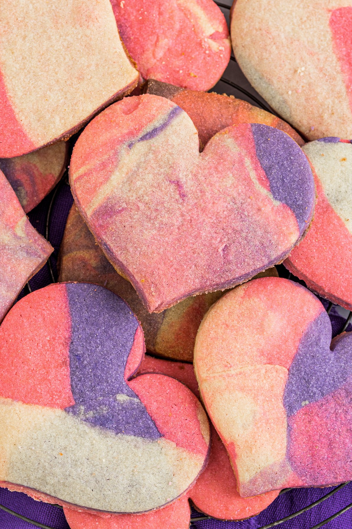 Heart shaped marbled sugar cookies on a cooling cookie rack with a purple napkin below.
