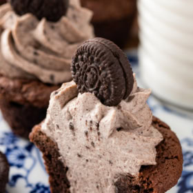 An Oreo cookie cup with cheesecake filling sliced in half on a blue and white plate.