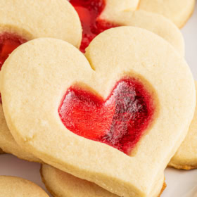 A Valentine's Day heart cookie stacked on top of more cookies on a white plate.
