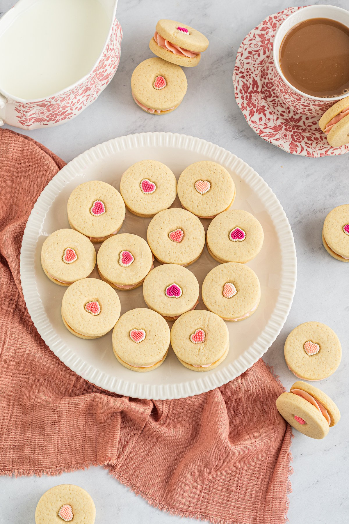Shortbread sandwich cookies with valentine sprinkles on top on a big white plate with a pink napkin.