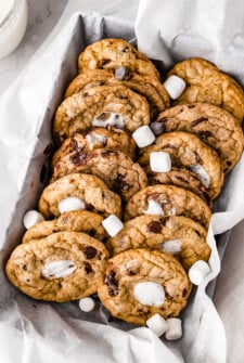 Two rows of chocolate chip cookies with marshmallows in a lined metal box.