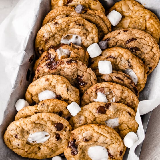 Two rows of chocolate chip cookies with marshmallows in a lined metal box.