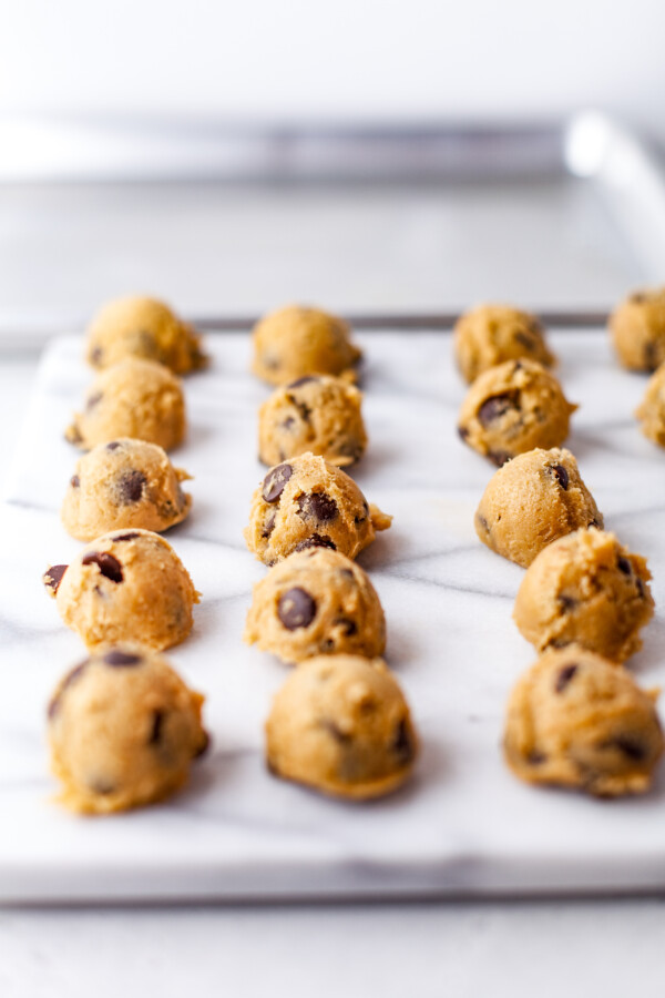 Balls of chocolate chip cookie dough on a parchment-lined baking sheet.