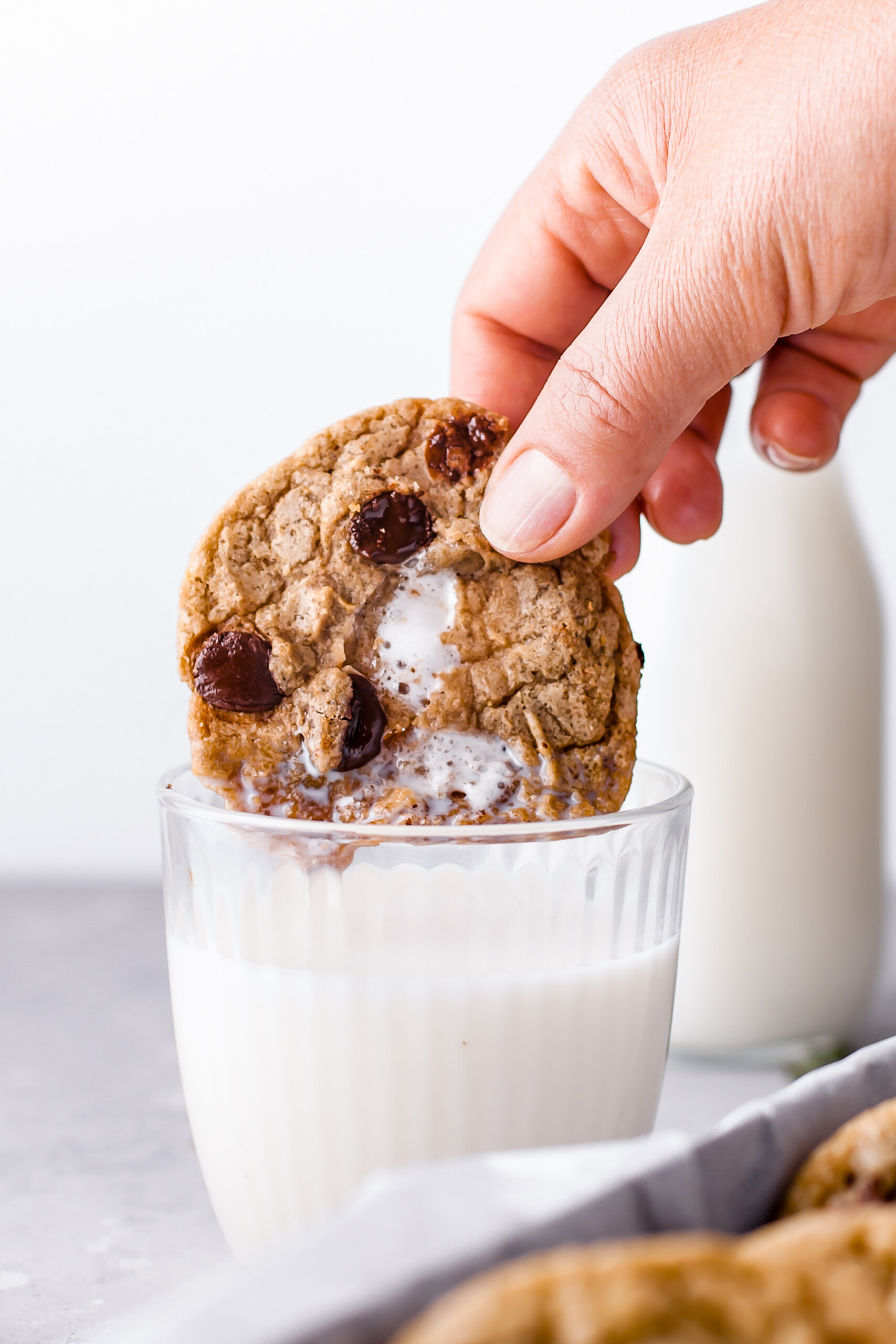 A woman's hand dipping a chocolate chip marshmallow cookie in a glass of milk.