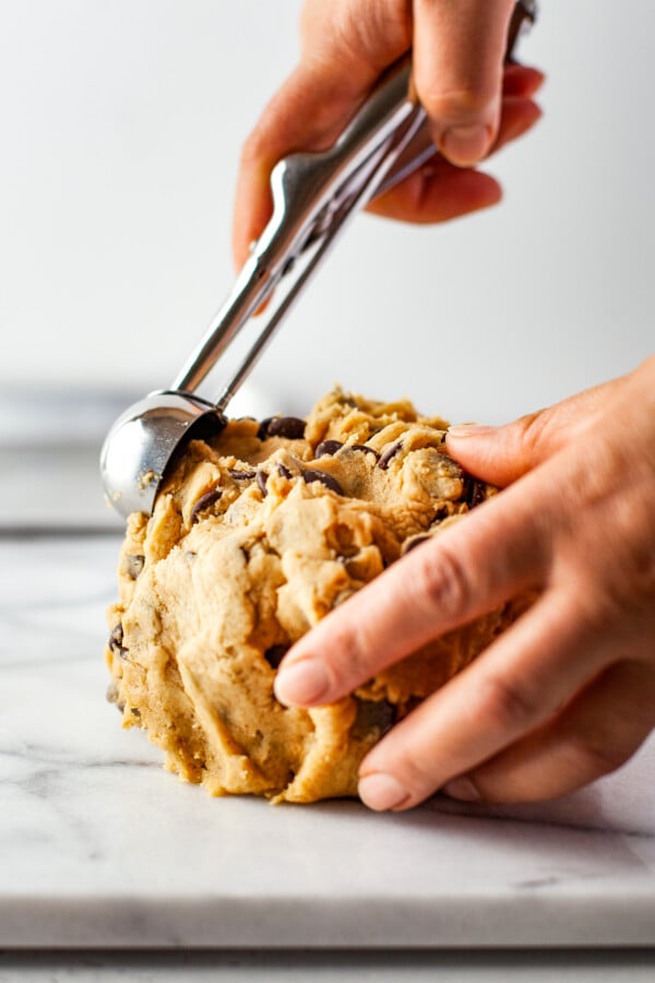 A woman uses a cookie scoop to portion a ball of cookie dough.