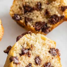 A chocolate chip muffin on a white plate sliced in half.