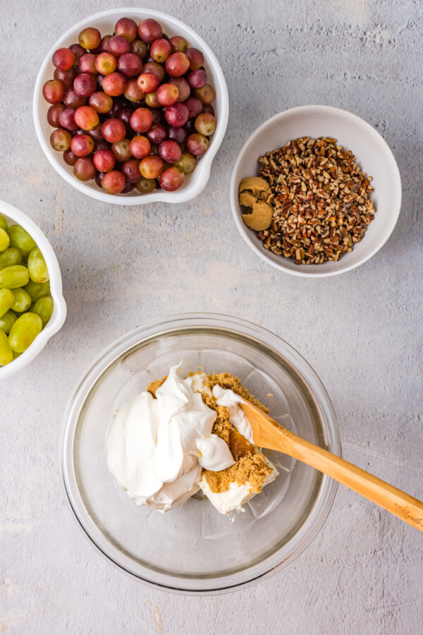 Mixing bowls with various ingredients. One bowl contains cream cheese and brown sugar, with a wooden spoon stuck in the cream cheese.