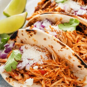 Close up shot of chicken tacos on a plate, topped with cheese and other toppings.