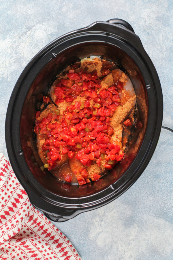 Overhead shot of a slow cooker with raw chicken and tomatoes.