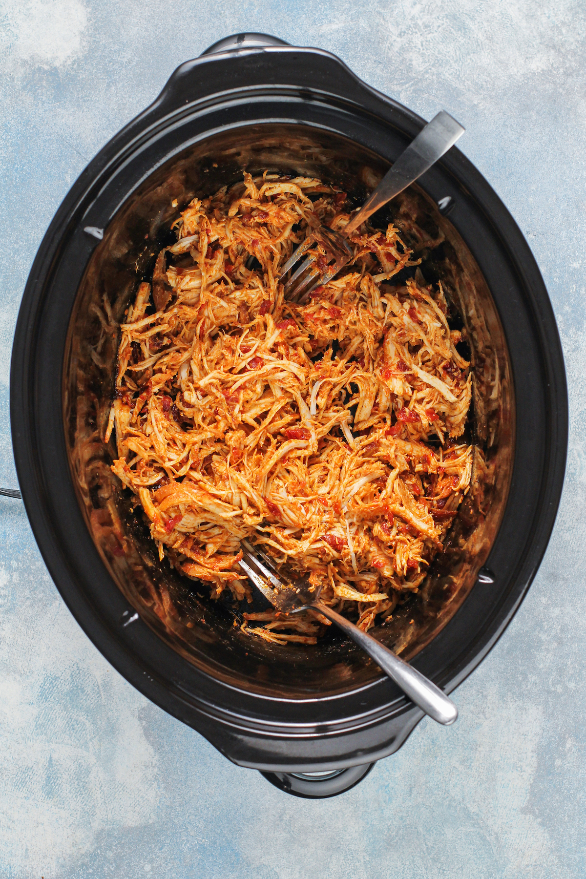 A slow cooker insert filled with cooked, seasoned, shredded chicken.