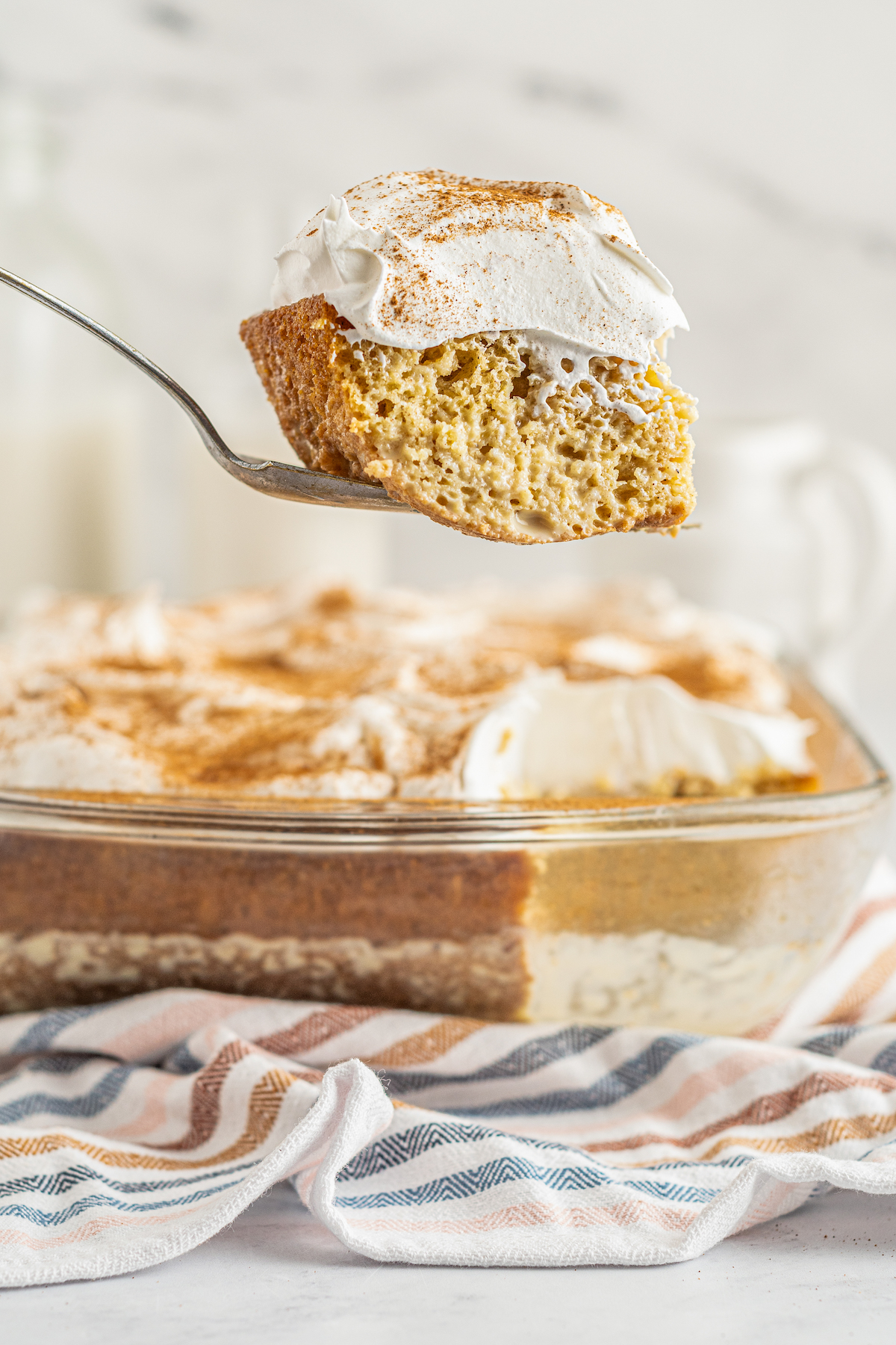 A slice of tres leches cake mix being lifted out of the baking dish with a cake server. 