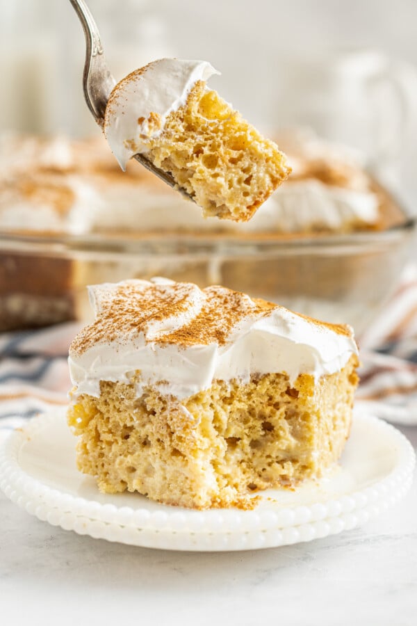 A slice of tres leches cake on a dessert plate with a fork lifting up one bite of the creamy chilled cake.