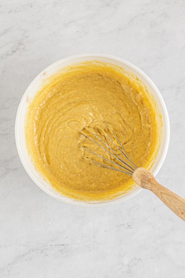 Cake batter in a mixing bowl being stirred with a whisk. 