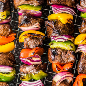 4 steak kabobs with vegetables on a cooling rack.