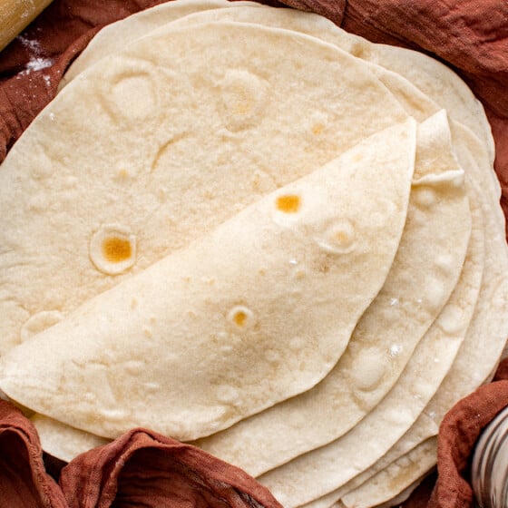 Homemade tortillas stacked on top of each other wrapped in a tea towel.