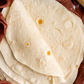 Flour tortillas stacked on top of each other wrapped in a tea towel.