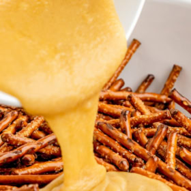 Honey mustard being poured into a bowl of pretzels.