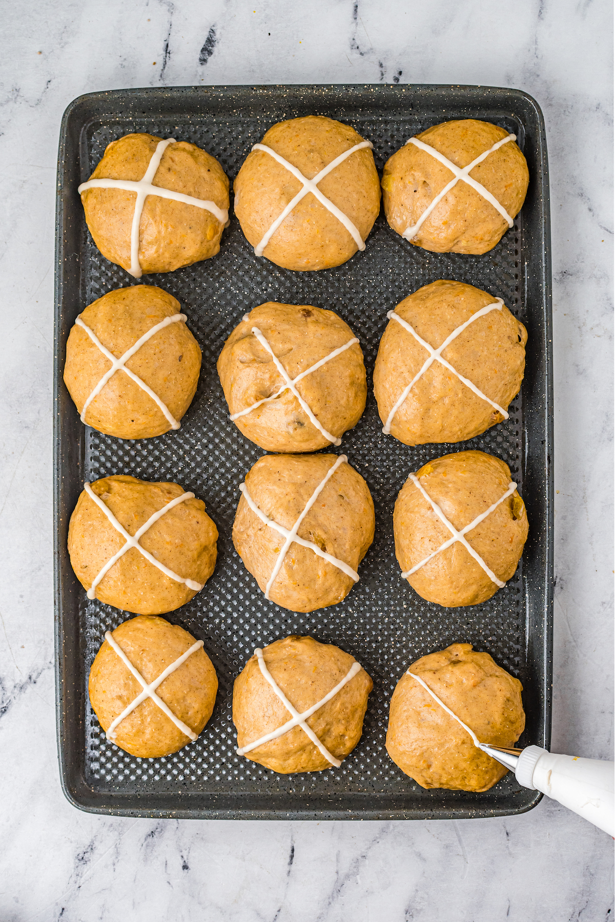 A dozen rolls with white crosses piped on top.