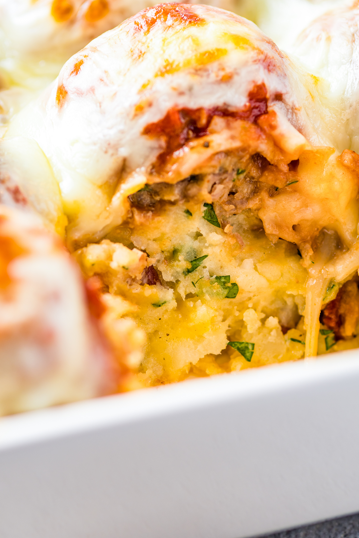 Close-up shot of a loaded mashed potato and meatball casserole, with one serving taken out to show texture.