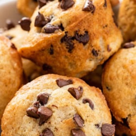 Mini chocolate chip muffins stacked on top of each other in a white bowl.