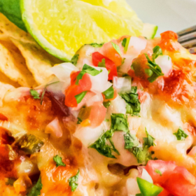 Pico de Gallo chicken with cheese on a white plate with tortilla chips and a lime wedge.