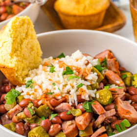 A bowl of red beans and rice, garnished with pickled okra an half a corn muffin.
