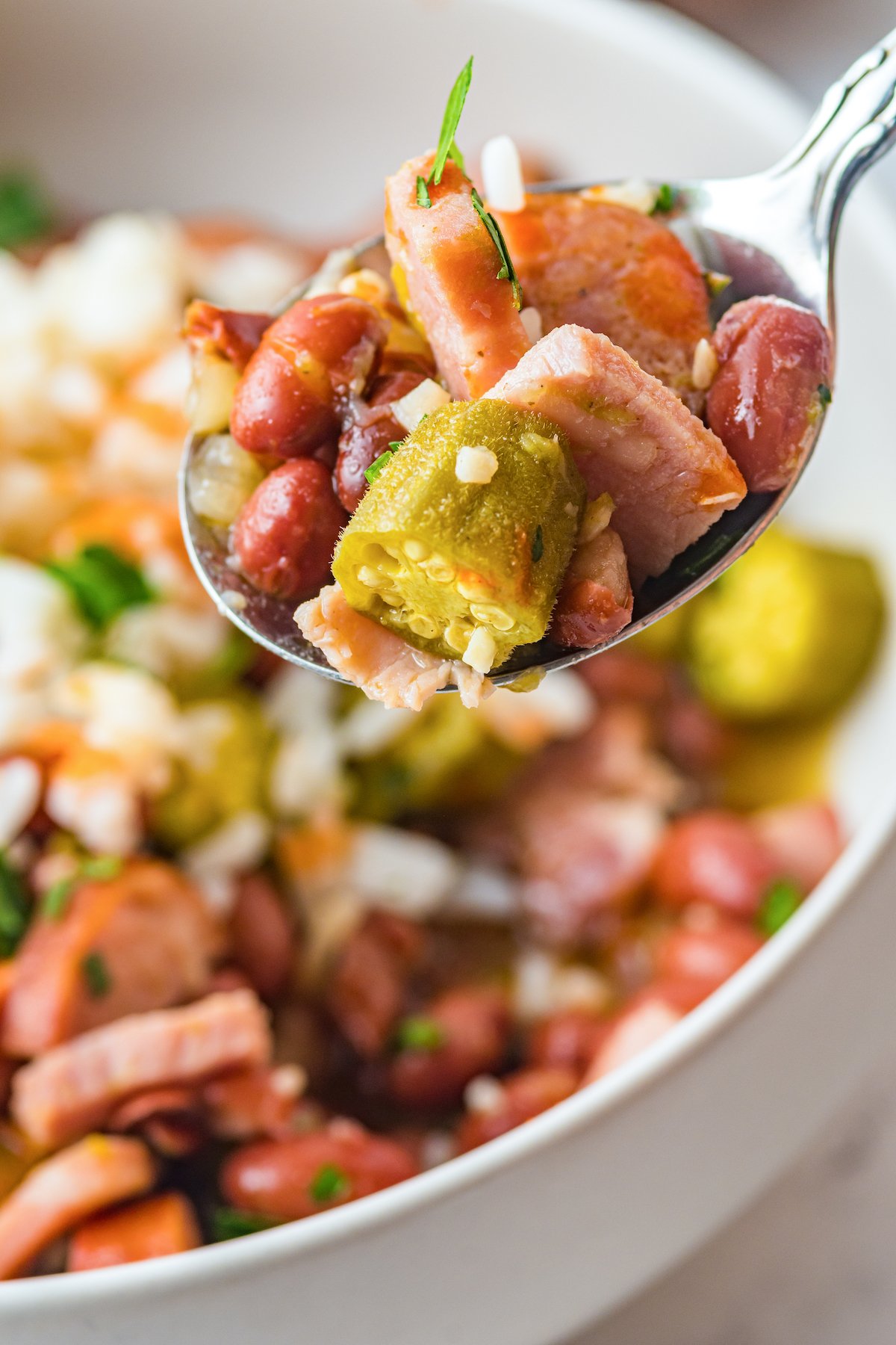 Close up shot of a spoonful of red beans, ham, sausage, and okra.