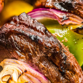 Up close image of a piece of grilled steak, onion and bell pepper on a kabob.