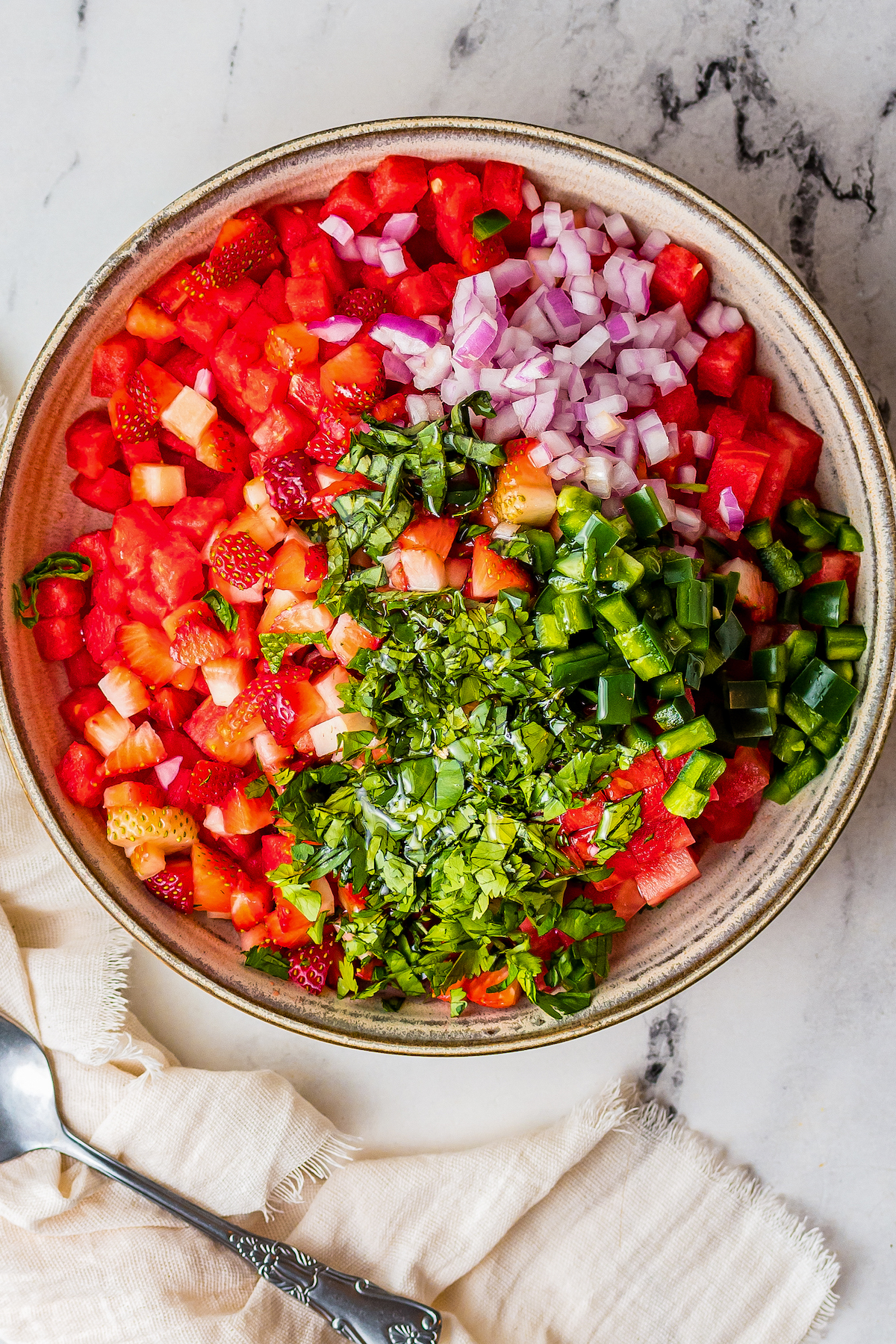 A bowl of chopped fruit with chopped fresh herbs, onion, and jalapeno.