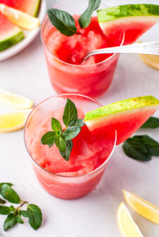 A frozen blended cocktail garnished with a thin watermelon slice, and fresh mint leaves.